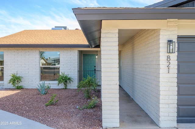 property entrance with a shingled roof and brick siding