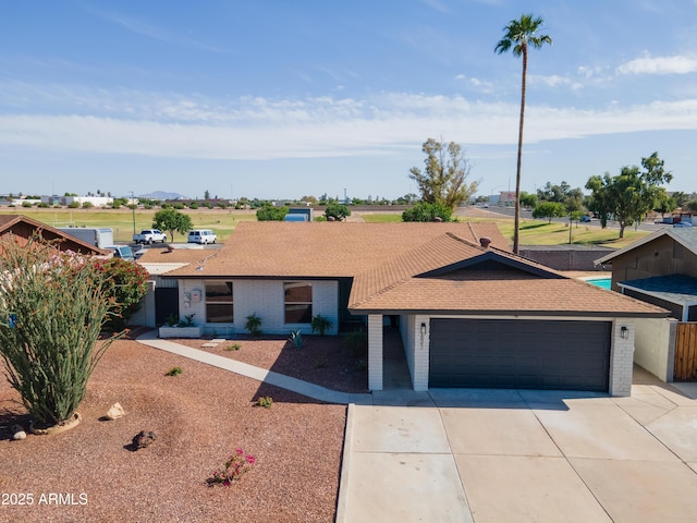 ranch-style house with concrete driveway, brick siding, an attached garage, and a shingled roof