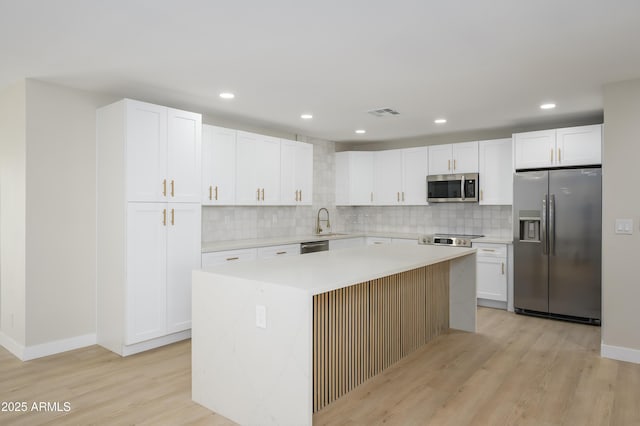 kitchen with light wood-type flooring, white cabinets, tasteful backsplash, a sink, and appliances with stainless steel finishes