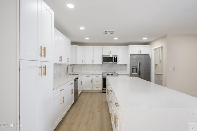kitchen with visible vents, appliances with stainless steel finishes, a center island, a sink, and white cabinets