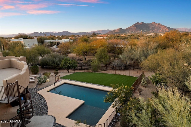 pool at dusk featuring a lawn, a patio area, and a mountain view