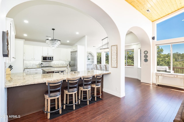 kitchen featuring a peninsula, dark wood-style flooring, appliances with stainless steel finishes, backsplash, and light stone countertops