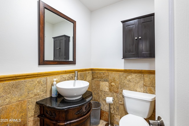 bathroom featuring toilet, wainscoting, vanity, and tile walls