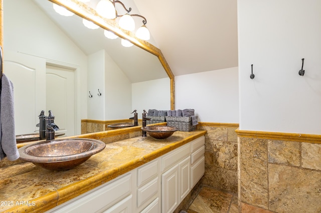 bathroom featuring lofted ceiling, tile walls, a sink, and wainscoting