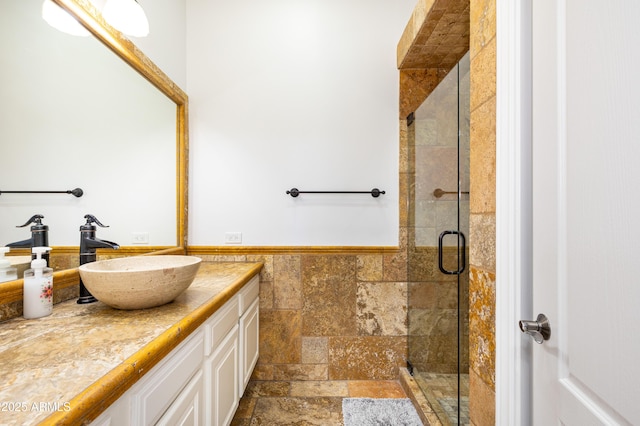 full bathroom with a wainscoted wall, vanity, tile walls, a shower stall, and stone tile flooring