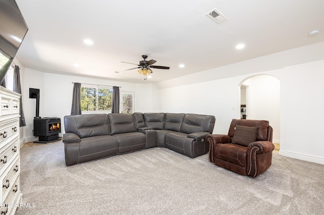 living area featuring arched walkways, recessed lighting, light carpet, visible vents, and a wood stove