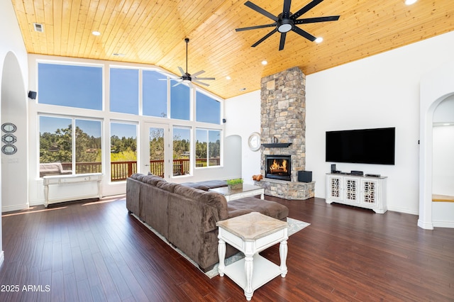 living room with arched walkways, dark wood finished floors, wood ceiling, a stone fireplace, and high vaulted ceiling