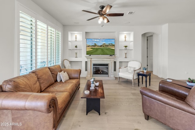 4279 N Spyglass Dr, Florence, AZ 85132 - living room with light wood finished floors, built in features, a ceiling fan, visible vents, and arched walkways