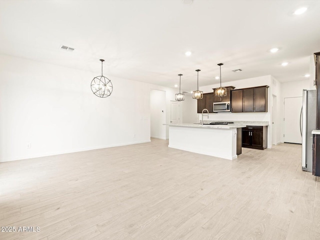 kitchen featuring dark brown cabinets, hanging light fixtures, appliances with stainless steel finishes, an island with sink, and light hardwood / wood-style floors