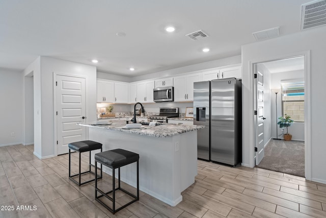 654 E Buckingham Ave, Gilbert, AZ 85297 - kitchen with appliances with stainless steel finishes, wood tiled floors, white cabinets, a breakfast bar, and light stone counters