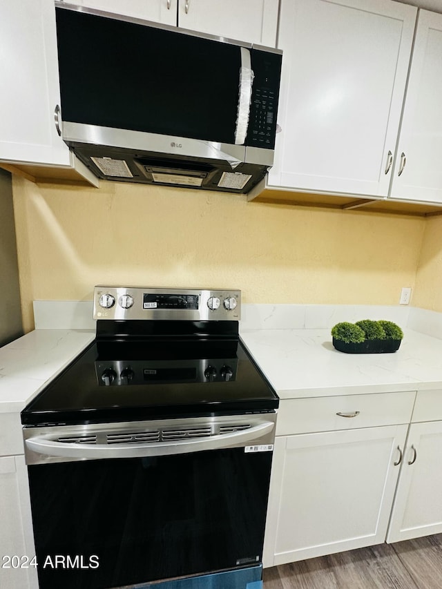 kitchen with light stone counters, hardwood / wood-style floors, white cabinets, and appliances with stainless steel finishes