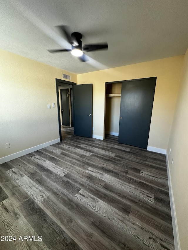 unfurnished bedroom with ceiling fan, a closet, dark wood-type flooring, and a textured ceiling