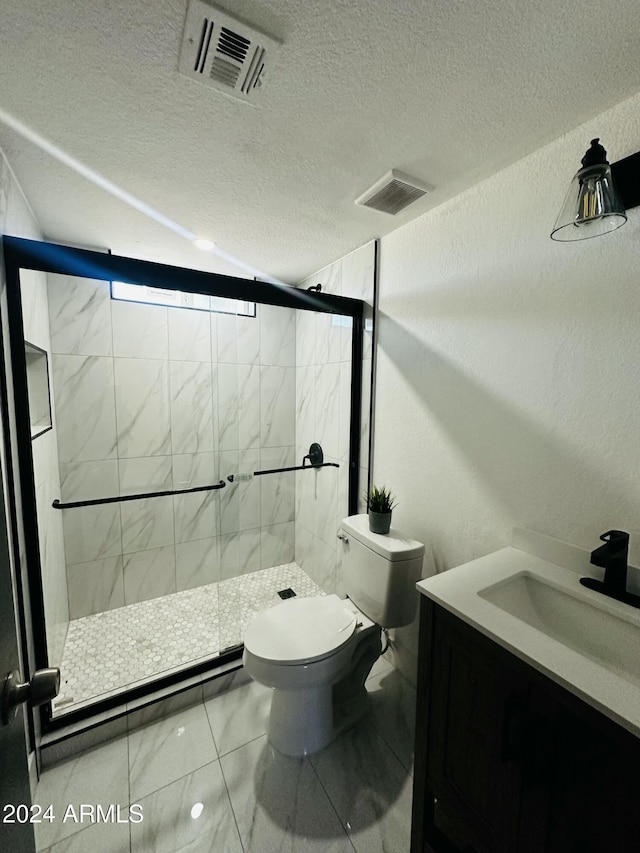 bathroom featuring vanity, toilet, a shower with shower door, and a textured ceiling