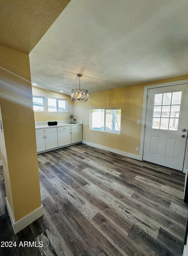 interior space with a healthy amount of sunlight, dark hardwood / wood-style flooring, a textured ceiling, and a chandelier