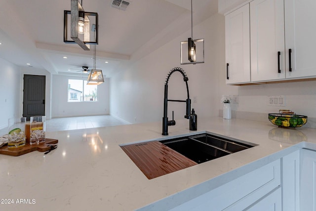 kitchen with light stone counters, sink, decorative light fixtures, and white cabinets