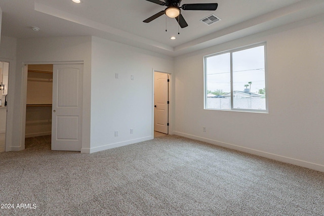 unfurnished bedroom with a walk in closet, light colored carpet, and ceiling fan