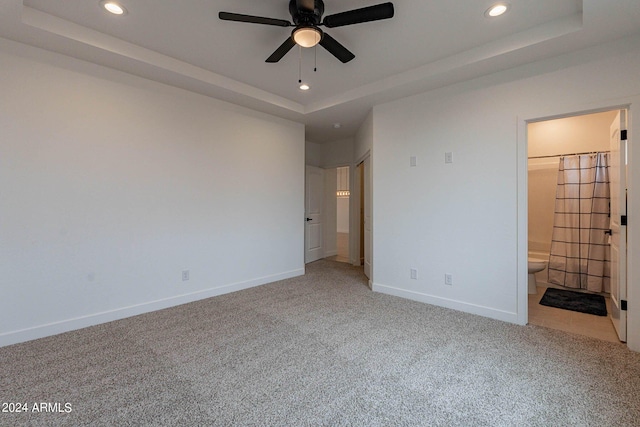 unfurnished bedroom featuring connected bathroom, ceiling fan, carpet flooring, and a tray ceiling