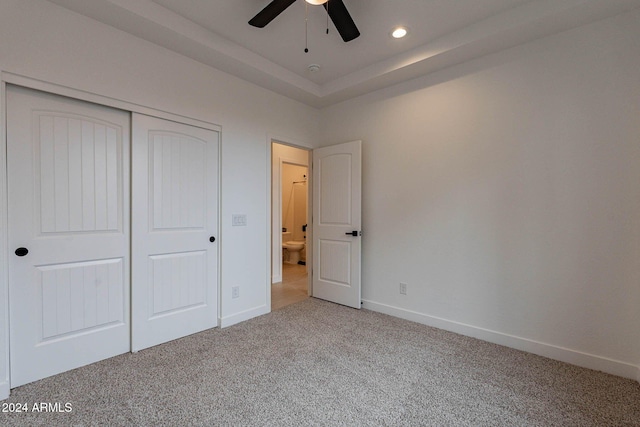 unfurnished bedroom with a tray ceiling, carpet flooring, a closet, and ceiling fan