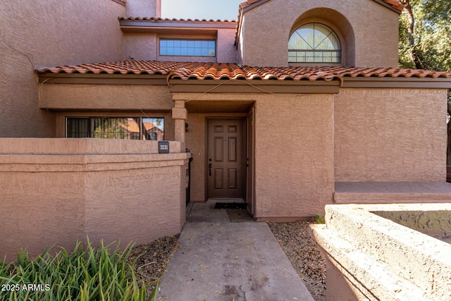 view of exterior entry with a tile roof, fence, and stucco siding