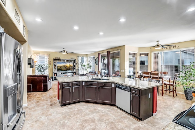 kitchen with stainless steel appliances, a kitchen island with sink, light stone countertops, and sink