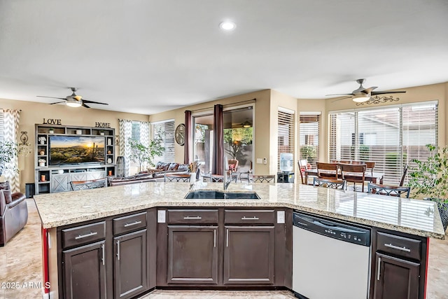 kitchen with light stone countertops, dishwasher, a kitchen island with sink, dark brown cabinets, and sink