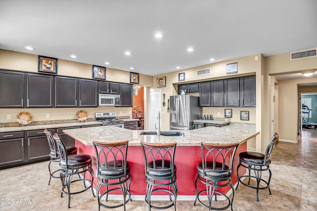 kitchen with stainless steel appliances, an island with sink, a kitchen bar, light stone counters, and sink