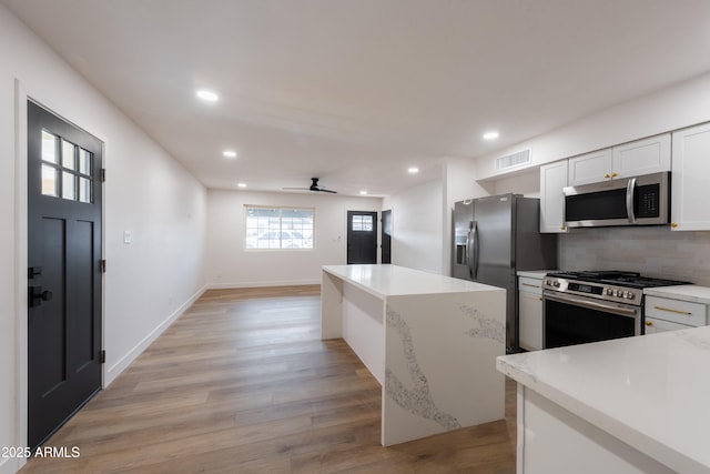 kitchen featuring white cabinetry, light wood-type flooring, ceiling fan, stainless steel appliances, and backsplash