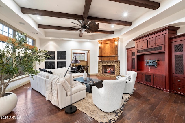 living room with beam ceiling, a large fireplace, ceiling fan, and dark wood-type flooring