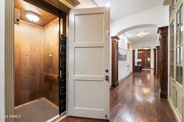 corridor featuring wood walls, ornate columns, dark wood-type flooring, and elevator