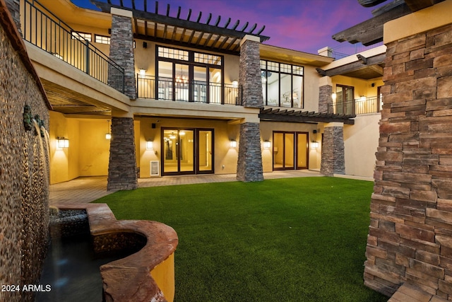 back house at dusk featuring a patio area, a balcony, and a yard