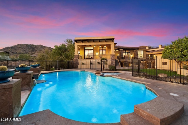 pool at dusk featuring a mountain view and an in ground hot tub