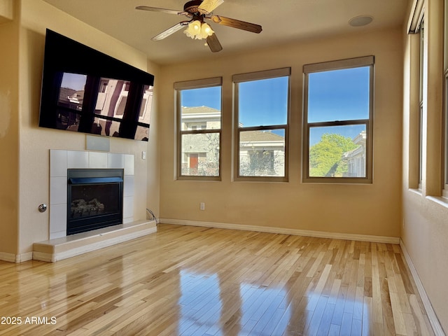 unfurnished living room with light hardwood / wood-style floors, a tile fireplace, and ceiling fan