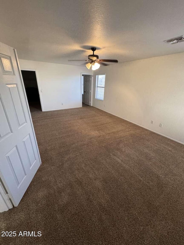 empty room with a textured ceiling, ceiling fan, and dark colored carpet