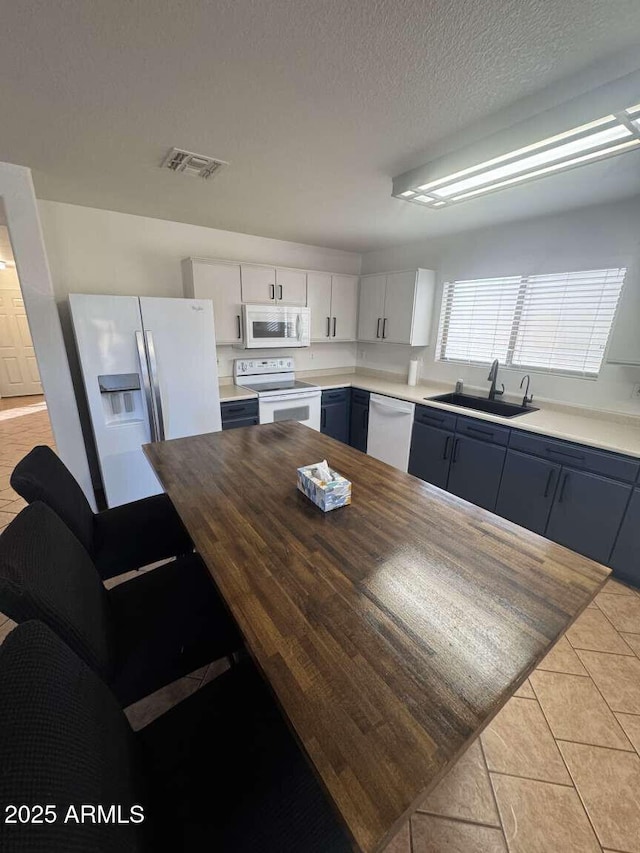 kitchen with white appliances, blue cabinetry, white cabinets, light tile patterned flooring, and sink