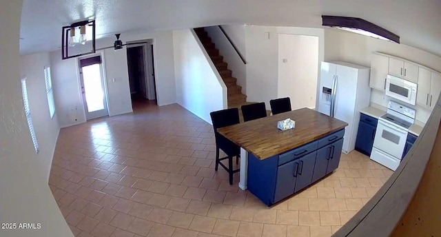 kitchen featuring white appliances, wooden counters, white cabinetry, blue cabinets, and a kitchen breakfast bar