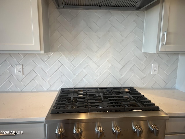 details featuring light stone counters, ventilation hood, range, and tasteful backsplash