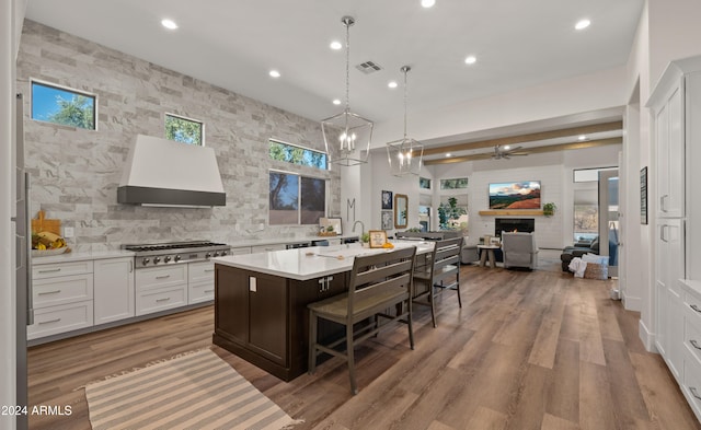 kitchen with stainless steel gas cooktop, custom exhaust hood, light countertops, open floor plan, and a warm lit fireplace