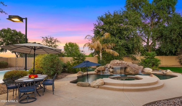 pool at dusk featuring a fenced in pool, a patio, a fenced backyard, an in ground hot tub, and outdoor dining area