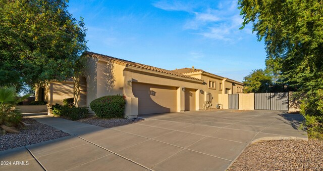 mediterranean / spanish home featuring an attached garage, a tile roof, driveway, a gate, and stucco siding