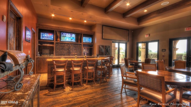 dining space with indoor wet bar, beamed ceiling, a towering ceiling, and hardwood / wood-style floors