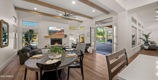 dining space featuring hardwood / wood-style flooring, beamed ceiling, a large fireplace, a towering ceiling, and ceiling fan