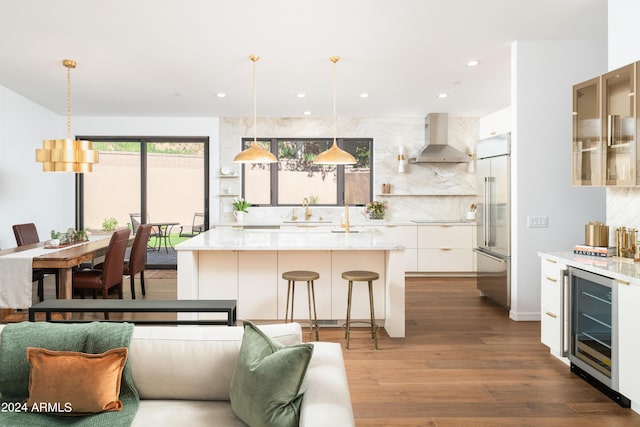 kitchen featuring beverage cooler, dark wood finished floors, built in refrigerator, wall chimney exhaust hood, and backsplash