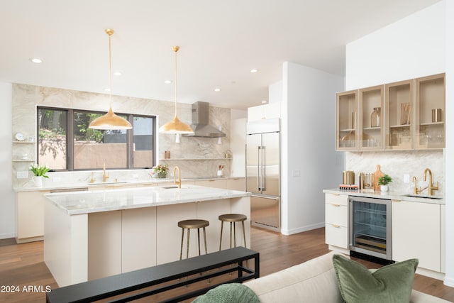 kitchen with wine cooler, wall chimney exhaust hood, built in refrigerator, and a sink