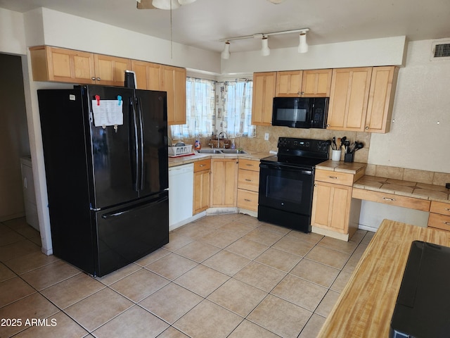 kitchen with light tile patterned floors, tile countertops, light brown cabinetry, black appliances, and a sink