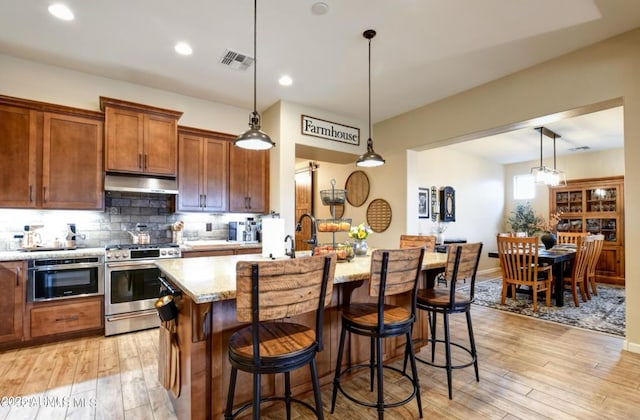 707 Lunar View Way, Chino Valley, AZ 86323 - kitchen with stainless steel appliances, under cabinet range hood, a breakfast bar, light stone counters, and light wood finished floors