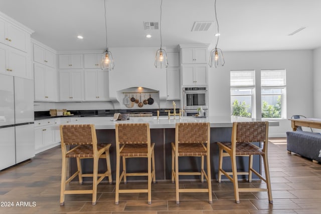 kitchen with a center island with sink, decorative light fixtures, white cabinetry, and a breakfast bar