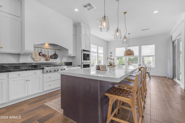 kitchen with appliances with stainless steel finishes, a breakfast bar, pendant lighting, a center island with sink, and white cabinets