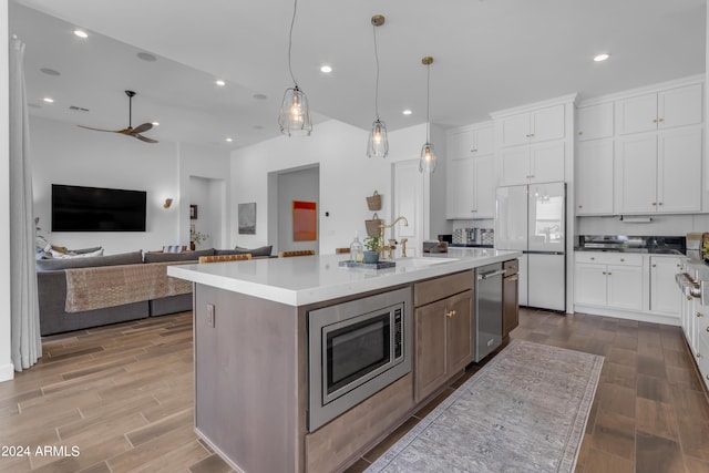 kitchen featuring fridge, a center island with sink, white cabinetry, and stainless steel microwave