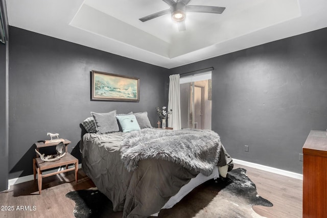 bedroom with a tray ceiling, ceiling fan, and light wood-type flooring