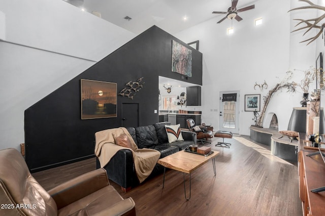 living room featuring ceiling fan, a fireplace, hardwood / wood-style floors, and a high ceiling